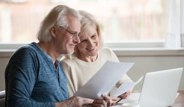 Happy aged husband and wife hold papers using laptop for online banking, satisfied senior couple smiling checking utility bills or insurance at computer with easy access, elderly users of technology